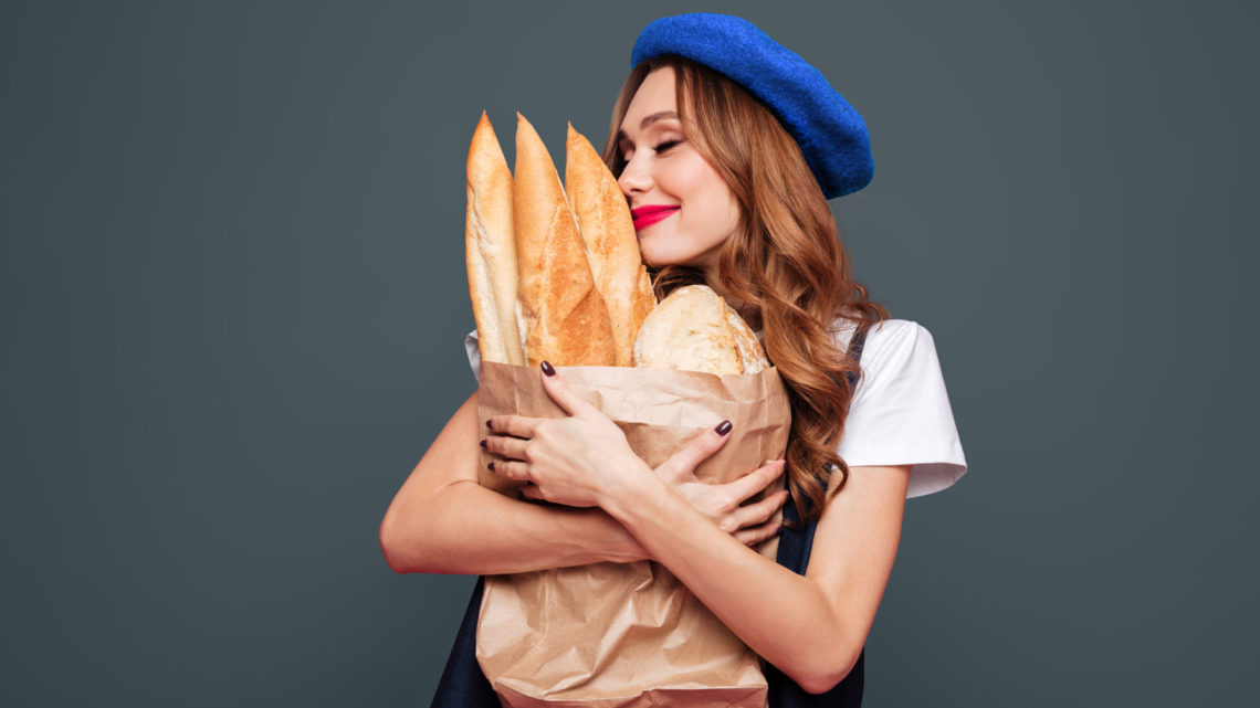 Young brunette happy lady in hat hug pack with baguettes and enjoy them isolated over pink